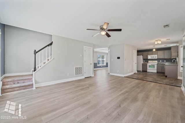 unfurnished living room with stairway, baseboards, visible vents, and light wood finished floors