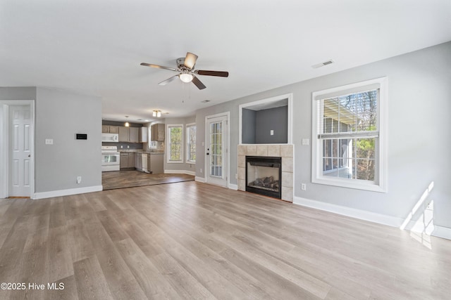 unfurnished living room featuring visible vents, light wood-style floors, a ceiling fan, a tile fireplace, and baseboards