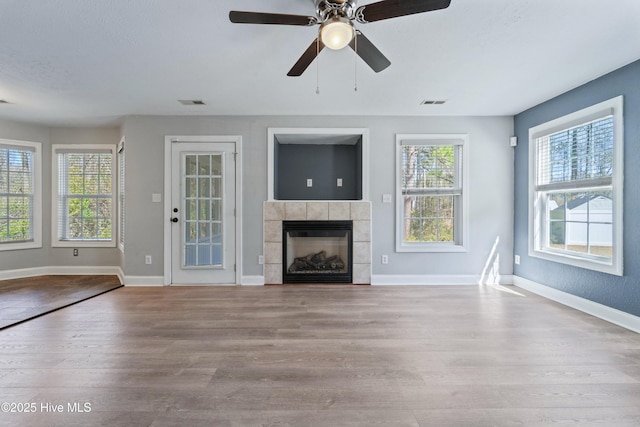 unfurnished living room with baseboards, visible vents, wood finished floors, and a tile fireplace