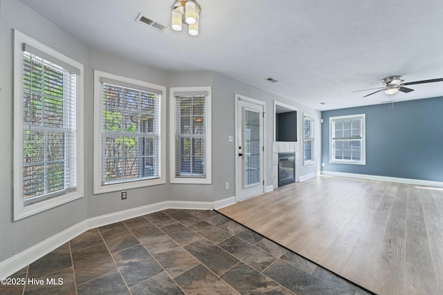 entryway with visible vents, a fireplace, baseboards, and a ceiling fan