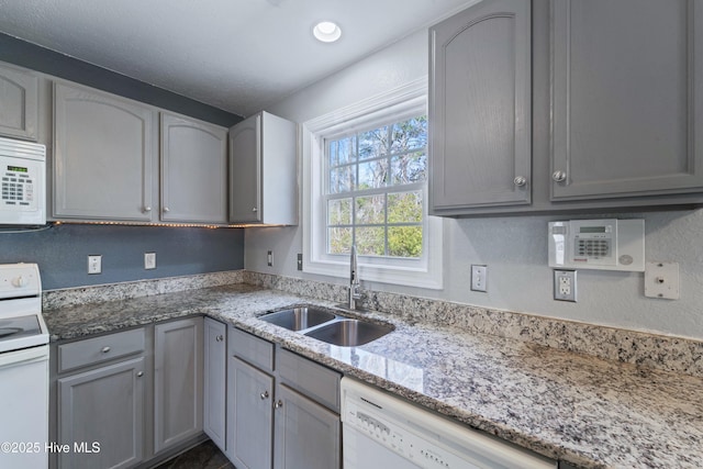 kitchen with gray cabinets, white appliances, a sink, and light stone countertops