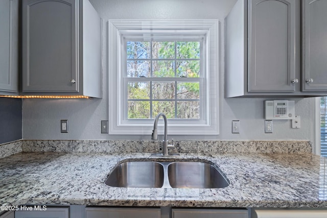 kitchen with light stone counters, a textured wall, gray cabinets, and a sink