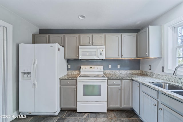 kitchen with light stone countertops, white appliances, and a sink