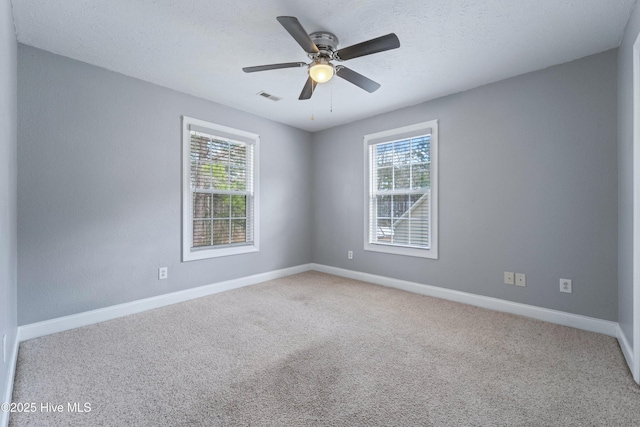 carpeted spare room with a ceiling fan, a wealth of natural light, visible vents, and baseboards