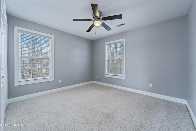 carpeted empty room featuring ceiling fan, visible vents, and baseboards