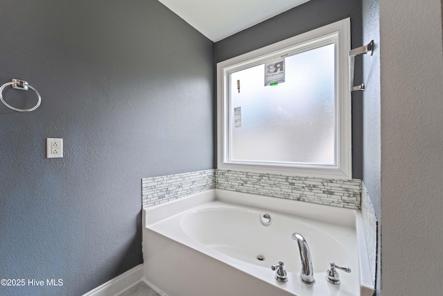 full bath featuring a textured wall, a bath, and baseboards