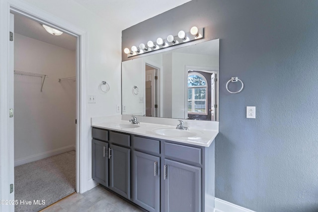 bathroom with a sink, a spacious closet, baseboards, and double vanity