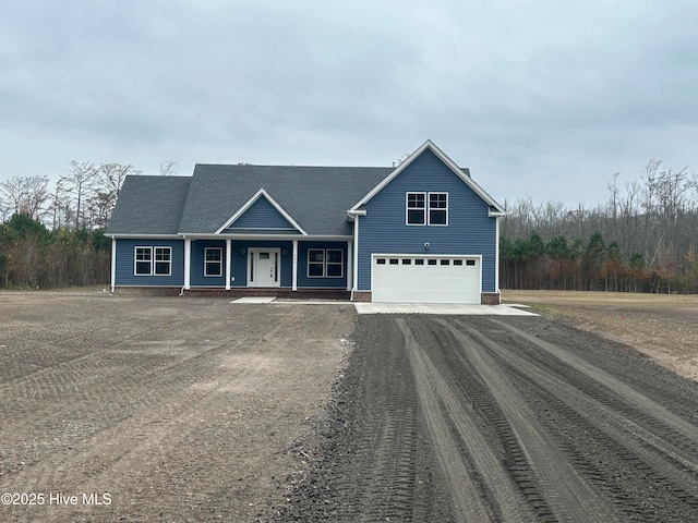 view of front facade with a garage, covered porch, and dirt driveway