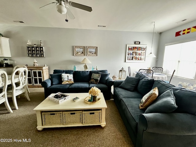 living room featuring dark colored carpet, visible vents, and ceiling fan