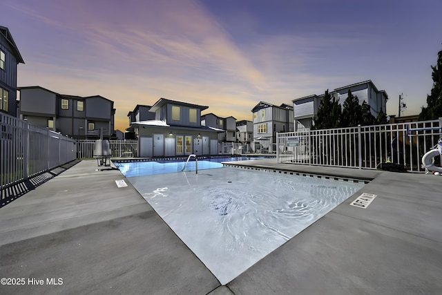 pool at dusk featuring a patio area, fence, and a community pool