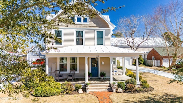 view of front facade featuring concrete driveway, metal roof, covered porch, a standing seam roof, and fence