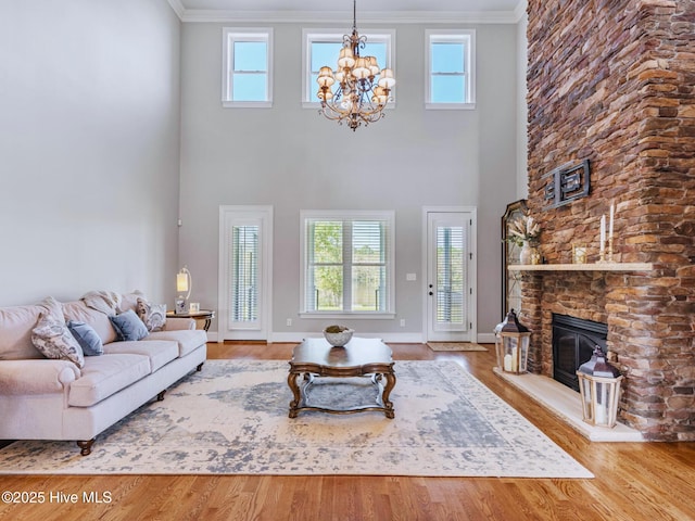 living area featuring a notable chandelier, ornamental molding, wood finished floors, a stone fireplace, and baseboards