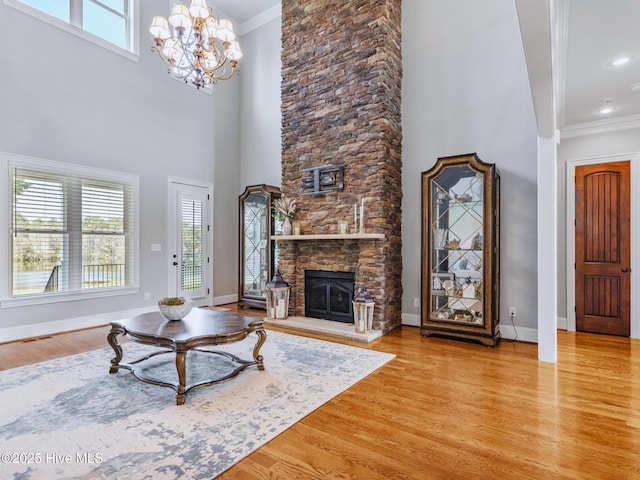 living room with a stone fireplace, crown molding, baseboards, and wood finished floors