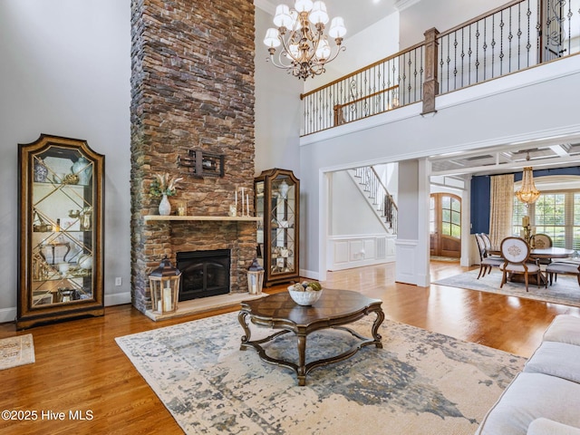 living area featuring a notable chandelier, stairway, a stone fireplace, and wood finished floors