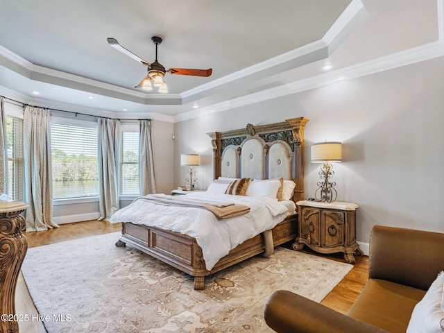 bedroom featuring wood finished floors, baseboards, a tray ceiling, recessed lighting, and crown molding