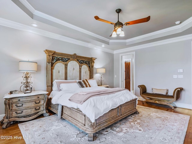 bedroom featuring a tray ceiling, wood finished floors, a ceiling fan, and ornamental molding