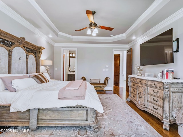 bedroom with dark wood finished floors, a tray ceiling, ornamental molding, and connected bathroom