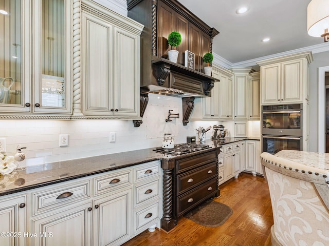 kitchen with ornamental molding, dark stone countertops, cream cabinets, light wood-style floors, and stainless steel appliances