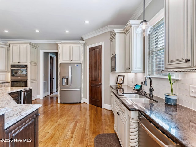 kitchen with dark stone counters, light wood-type flooring, cream cabinetry, stainless steel appliances, and a sink