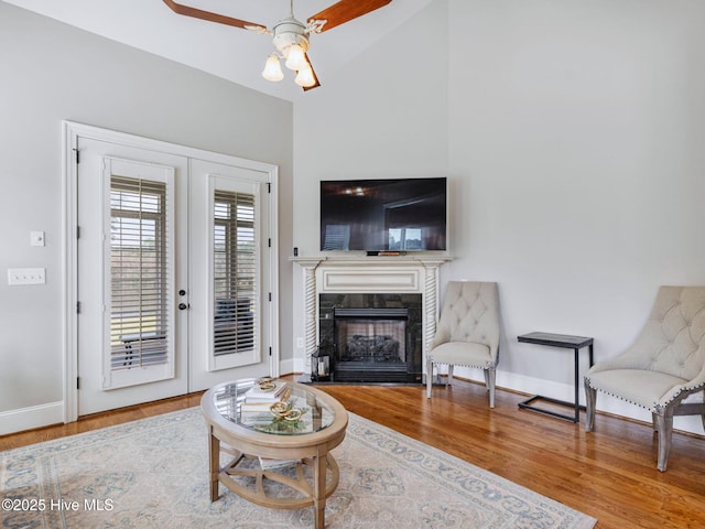 living area with a fireplace with flush hearth, wood finished floors, french doors, baseboards, and ceiling fan