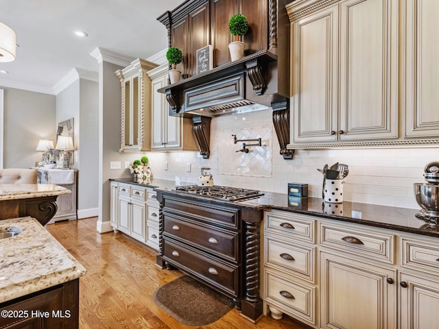 kitchen with light wood-type flooring, cream cabinetry, ornamental molding, dark stone countertops, and tasteful backsplash