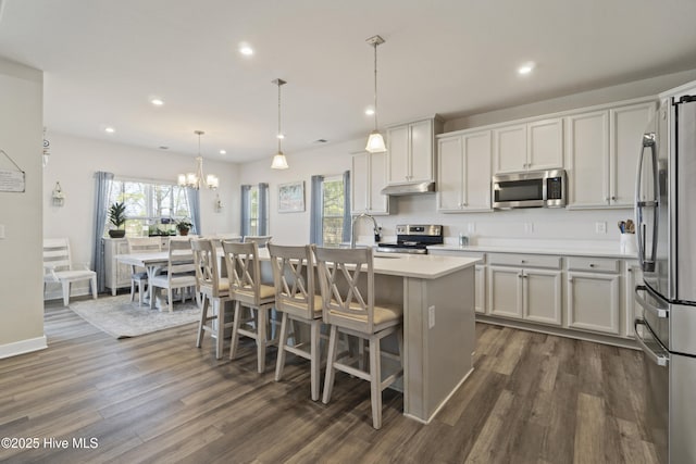 kitchen with under cabinet range hood, a sink, appliances with stainless steel finishes, light countertops, and dark wood-style flooring