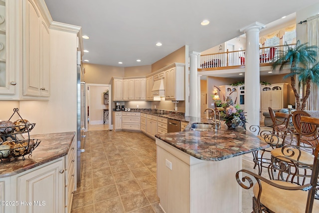 kitchen with a sink, a peninsula, decorative columns, dishwasher, and a breakfast bar area
