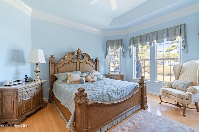 bedroom featuring light wood finished floors, ornamental molding, baseboards, and a raised ceiling
