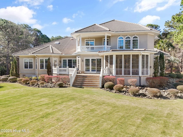 rear view of property featuring a balcony, a lawn, stairs, stucco siding, and a tile roof