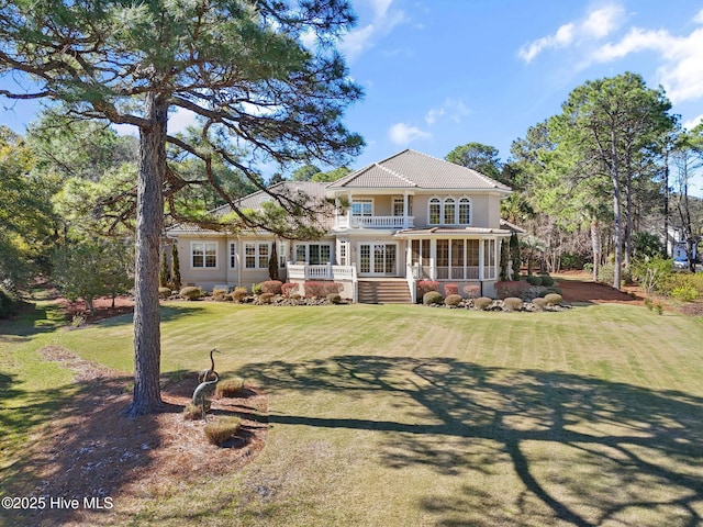 rear view of house with a balcony, a sunroom, a lawn, and french doors