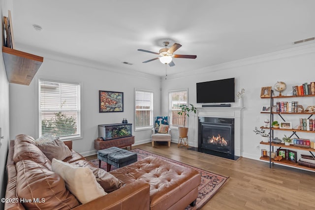 living area featuring ornamental molding, a glass covered fireplace, visible vents, and wood finished floors