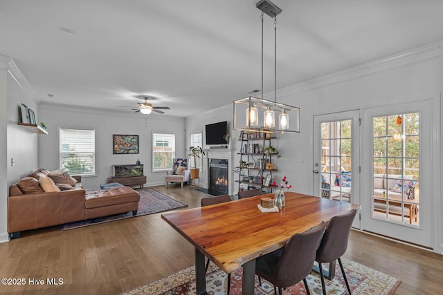 dining room with baseboards, a fireplace with flush hearth, ceiling fan, ornamental molding, and wood finished floors