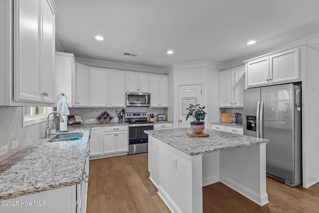 kitchen with stainless steel appliances, a sink, white cabinetry, visible vents, and a center island