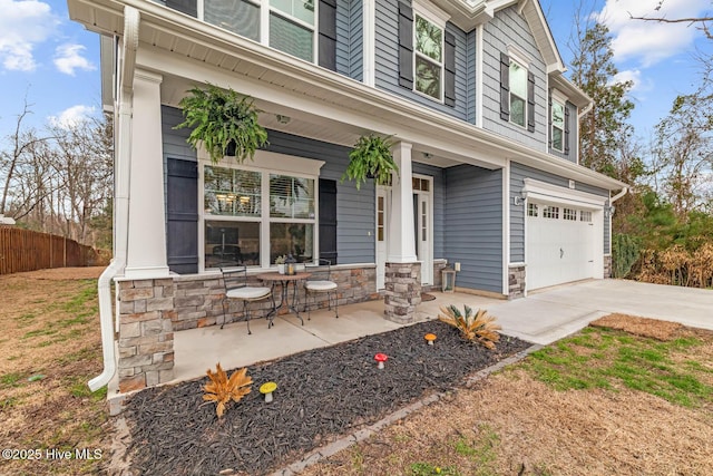 view of front of home featuring an attached garage, covered porch, fence, stone siding, and concrete driveway