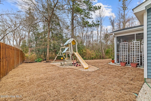 view of jungle gym featuring a sunroom, fence, and a lawn