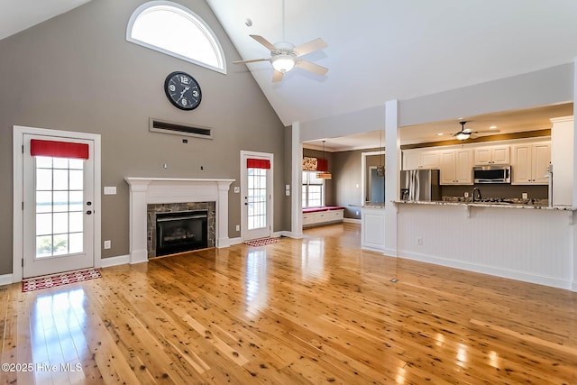 unfurnished living room featuring a ceiling fan, light wood-style floors, a fireplace, high vaulted ceiling, and a sink