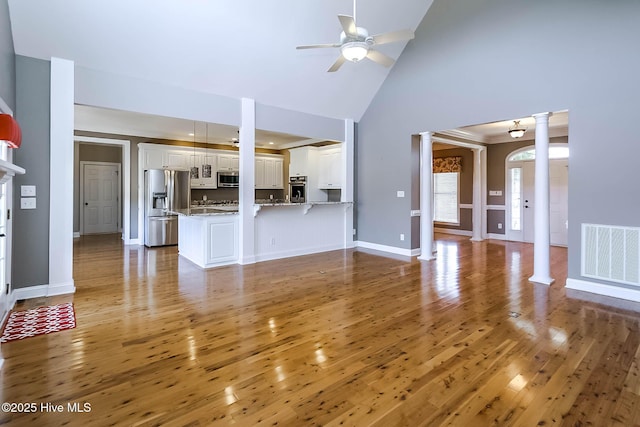 unfurnished living room featuring visible vents, light wood-style floors, ceiling fan, ornate columns, and high vaulted ceiling