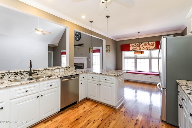 kitchen featuring white cabinets, stainless steel appliances, crown molding, light wood-type flooring, and a sink