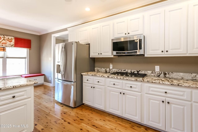 kitchen with appliances with stainless steel finishes, light stone counters, crown molding, light wood-type flooring, and white cabinetry