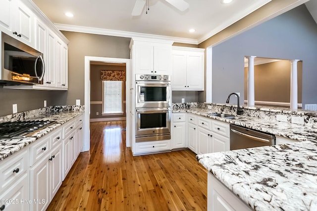 kitchen featuring light wood finished floors, decorative columns, stainless steel appliances, crown molding, and a sink