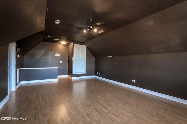 bonus room with lofted ceiling, wood finished floors, visible vents, a ceiling fan, and baseboards