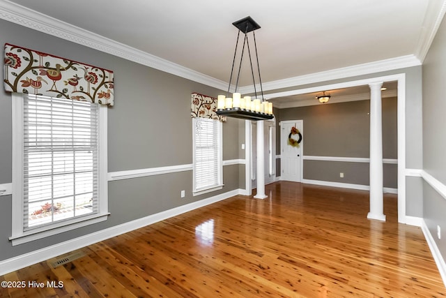 unfurnished dining area with ornate columns, crown molding, baseboards, and wood finished floors