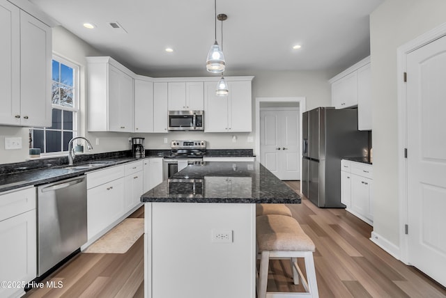 kitchen featuring a kitchen island, a breakfast bar area, appliances with stainless steel finishes, white cabinetry, and a sink