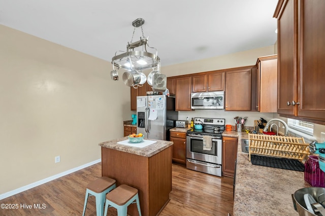 kitchen featuring baseboards, appliances with stainless steel finishes, wood finished floors, a center island, and light countertops