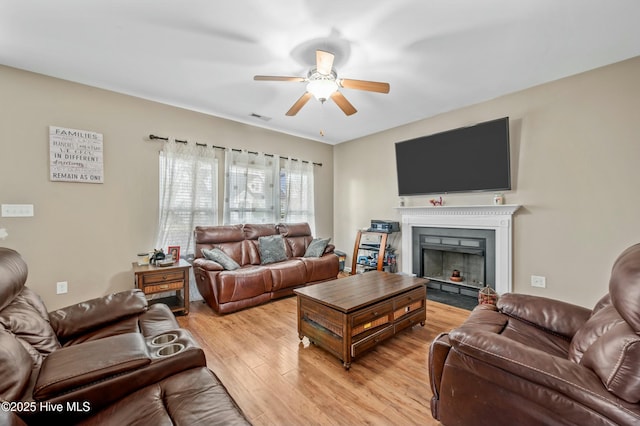 living room with a fireplace with flush hearth, visible vents, light wood finished floors, and a ceiling fan