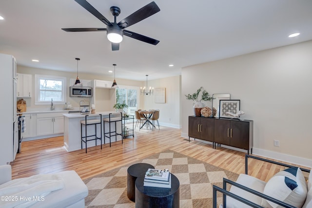 living area with light wood-type flooring, ceiling fan with notable chandelier, baseboards, and recessed lighting