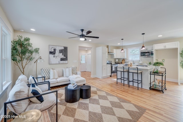 living area featuring baseboards, light wood finished floors, a ceiling fan, and recessed lighting