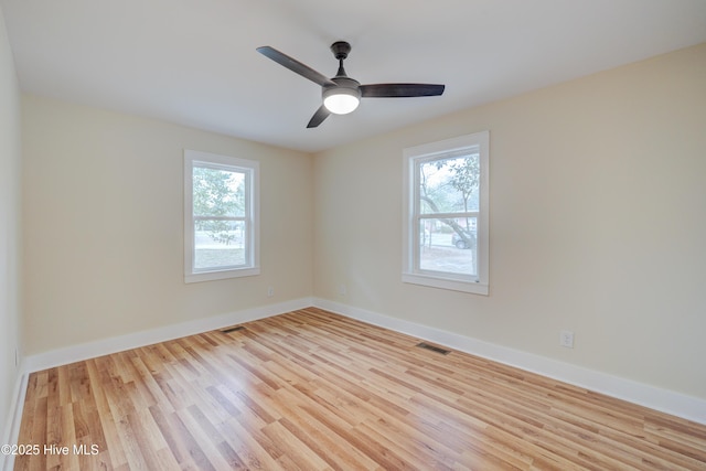 unfurnished room featuring baseboards, wood finished floors, visible vents, and a healthy amount of sunlight