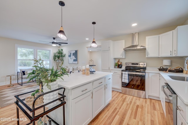 kitchen with appliances with stainless steel finishes, white cabinetry, light wood finished floors, and wall chimney exhaust hood