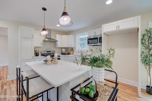 kitchen featuring stainless steel appliances, light countertops, white cabinetry, a sink, and wall chimney exhaust hood